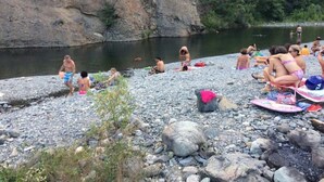 Ein felsiger Flussufer mit Menschen, die sonnenbaden und schwimmen.