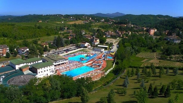 Eine Vogelperspektive zeigt ein Resort mit einem großen Schwimmbecken, Wasserrutschen und einem mehrstöckigen Gebäude.