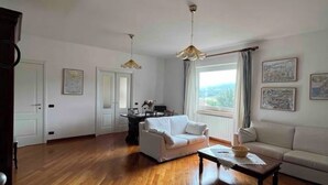 Ein geräumiges Wohnzimmer mit Holzdielen, einem weißen Sofa, einem Couchtisch und einem Essbereich mit Tisch und Stühlen.