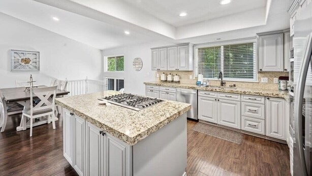 A modern kitchen with white cabinetry, granite countertops, and a central island with a stove. - Cedar Falls Retreat: Beachfront 5BR Home w/ Community Beach Access (Post Falls)