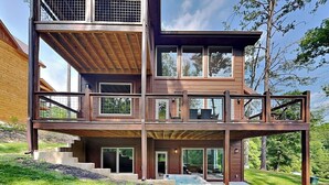 A multi-story wooden house with a balcony, large windows, and a hot tub. - Smoky Poolside Chalet by Smoky Cove Resort (Sevierville)