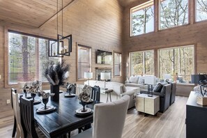 A spacious living room with a fireplace, large windows, and a dining area with a wooden table and chairs. - Smoky Poolside Chalet by Smoky Cove Resort (Sevierville)