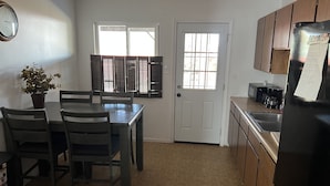 A kitchen with a dining table, chairs, a refrigerator, a microwave, and a sink. - Home on Yucca (El Centro)
