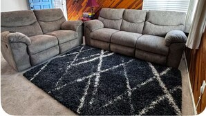A living room with two grey sofas, a black and white rug, a wooden wall, a blue door, and a lamp. - Home on Yucca (El Centro)
