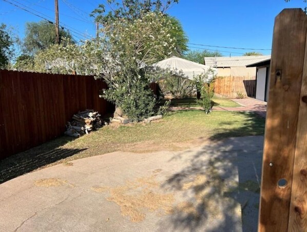 A backyard with a wooden fence, a covered patio, and a small tree. - Home on Yucca (El Centro)