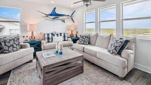 A spacious living room with a large window, a ceiling fan, and a decorative fish wall hanging. - Blue Fin by Ryson Vacation Rentals (Freeport)