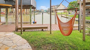 A wooden deck with a hammock, a view of a canal, and a stone pathway. - Blue Fin by Ryson Vacation Rentals (Freeport)
