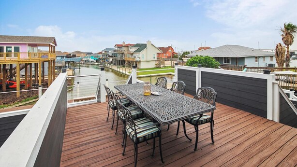 A wooden deck with a table and chairs, overlooking a marina with boats and houses. - Blue Fin by Ryson Vacation Rentals (Freeport)