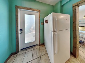 Compact kitchen with a refrigerator, door, and beige tile flooring.