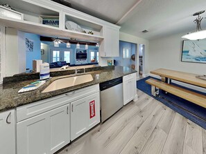 A modern kitchen with a granite countertop, white cabinetry, and a built-in dishwasher. - Sea Breeze Escape by Silver Sands Vacation Rentals (Port Aransas)