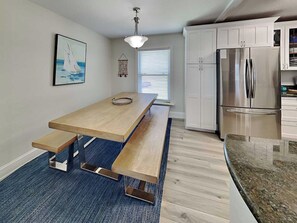 Uma cozinha moderna com uma mesa de madeira, armários embutidos, uma geladeira de aço inoxidável e um tapete azul.