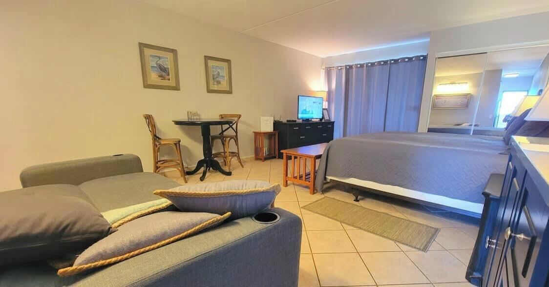 A hotel room with a bed, a sofa, a desk with a computer, and two chairs.