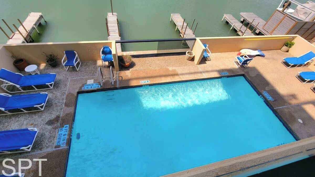 Una piscina en la azotea con sillas reclinables azules, una mesita y una planta en maceta.