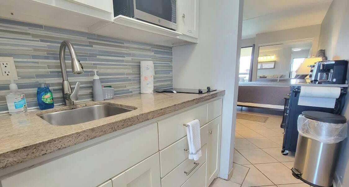 A modern kitchen with a granite countertop, stainless steel sink, and white cabinetry. There is a microwave above the sink, and a coffee machine on the right.