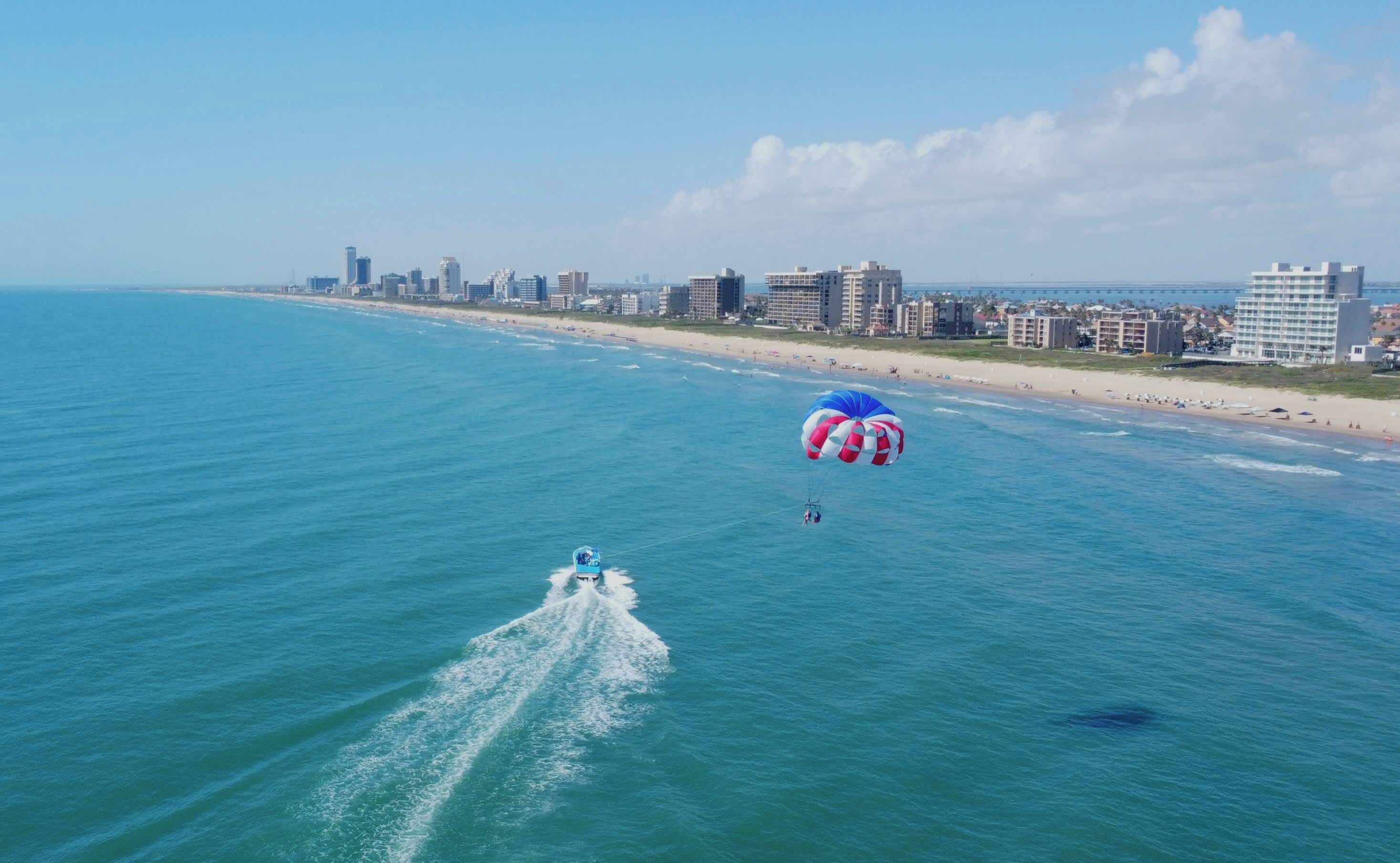 Un paisaje urbano costero con playa, edificios altos y un paracaídas en el agua.