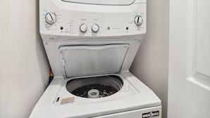 A front view of a white washer and dryer unit with control knobs for temperature, load size, and spin speed. - Peggy's Hideaway by Ryson Vacation Rentals (Galveston)