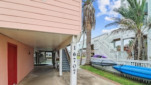 A covered walkway with a red door, a staircase, and a building with a white railing. - Peggy's Hideaway by Ryson Vacation Rentals (Galveston)