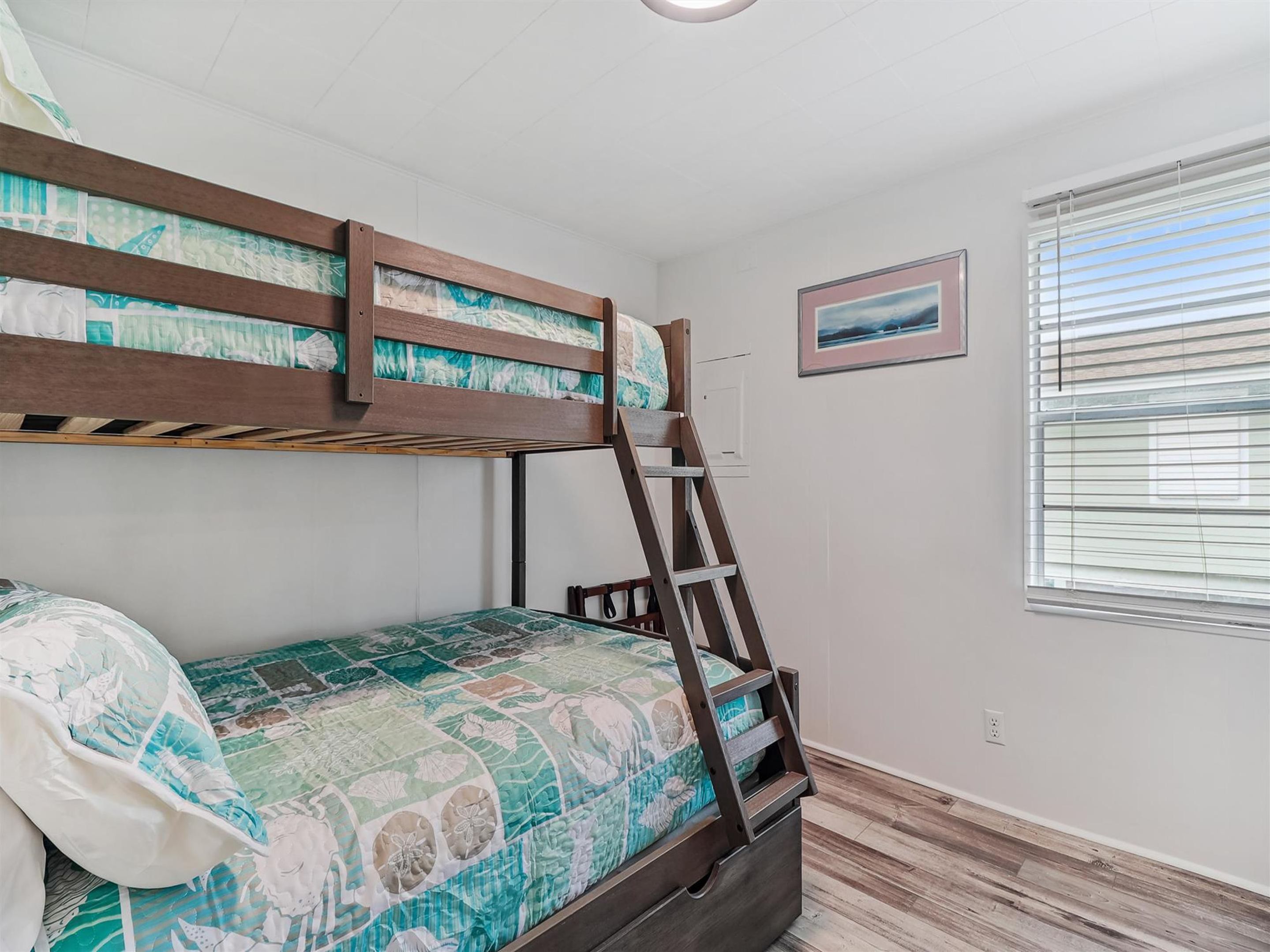 A bunk bed with a ladder, a quilted bedspread, and a window with blinds.