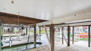 A boat docked under a covered area with a view of a waterway and buildings in the background. - Peggy's Hideaway by Ryson Vacation Rentals (Galveston)