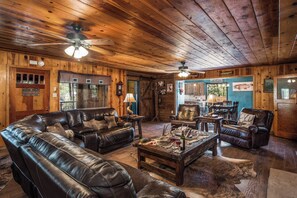 A rustic interior with a leather sofa, wooden ceiling, and a dining area. - The Roost Downtown by Ruidoso Vacation Rentals (Ruidoso)
