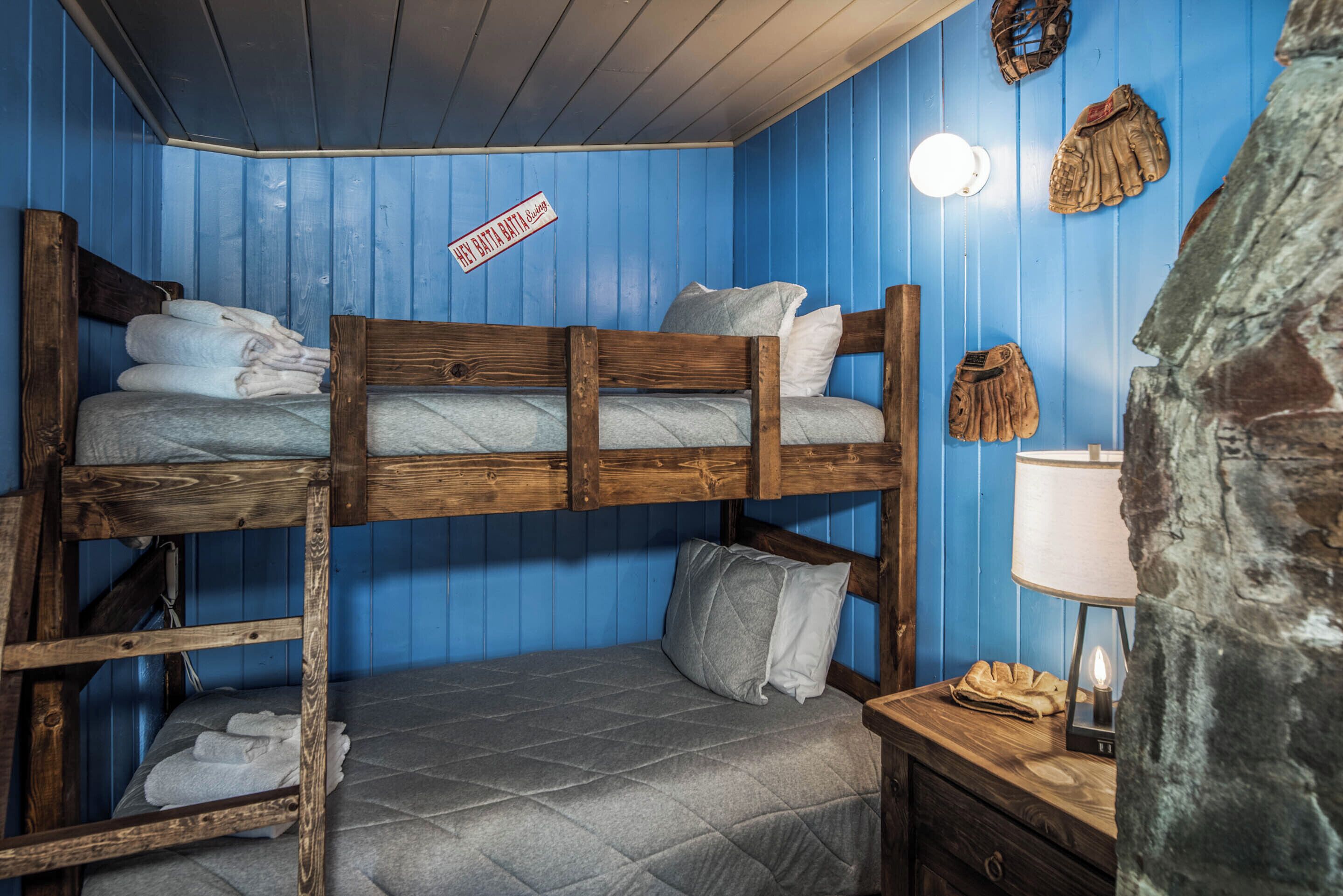 A bunk bed room with blue walls, a wooden headboard, and a nightstand with a lamp.