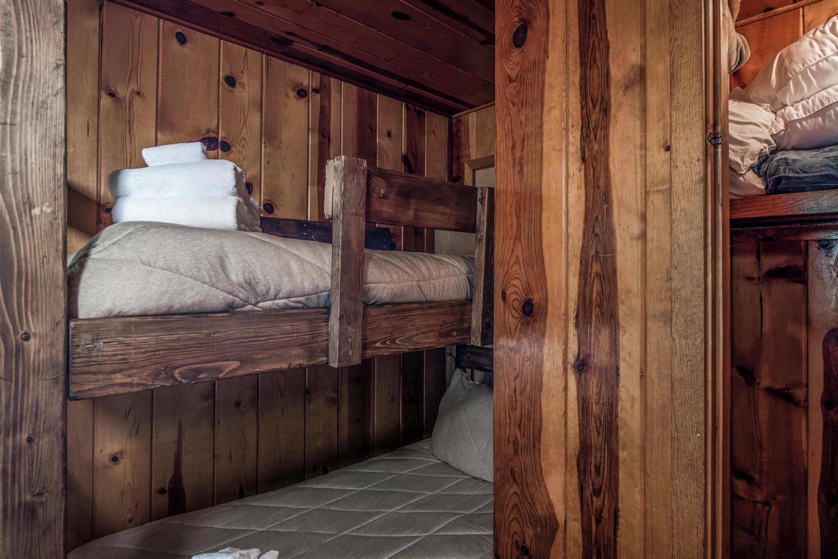 A bunk bed with a wooden headboard, a lower bunk with a pillow, and a mattress.