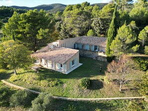 A two-story house with a tiled roof, surrounded by lush greenery and trees.