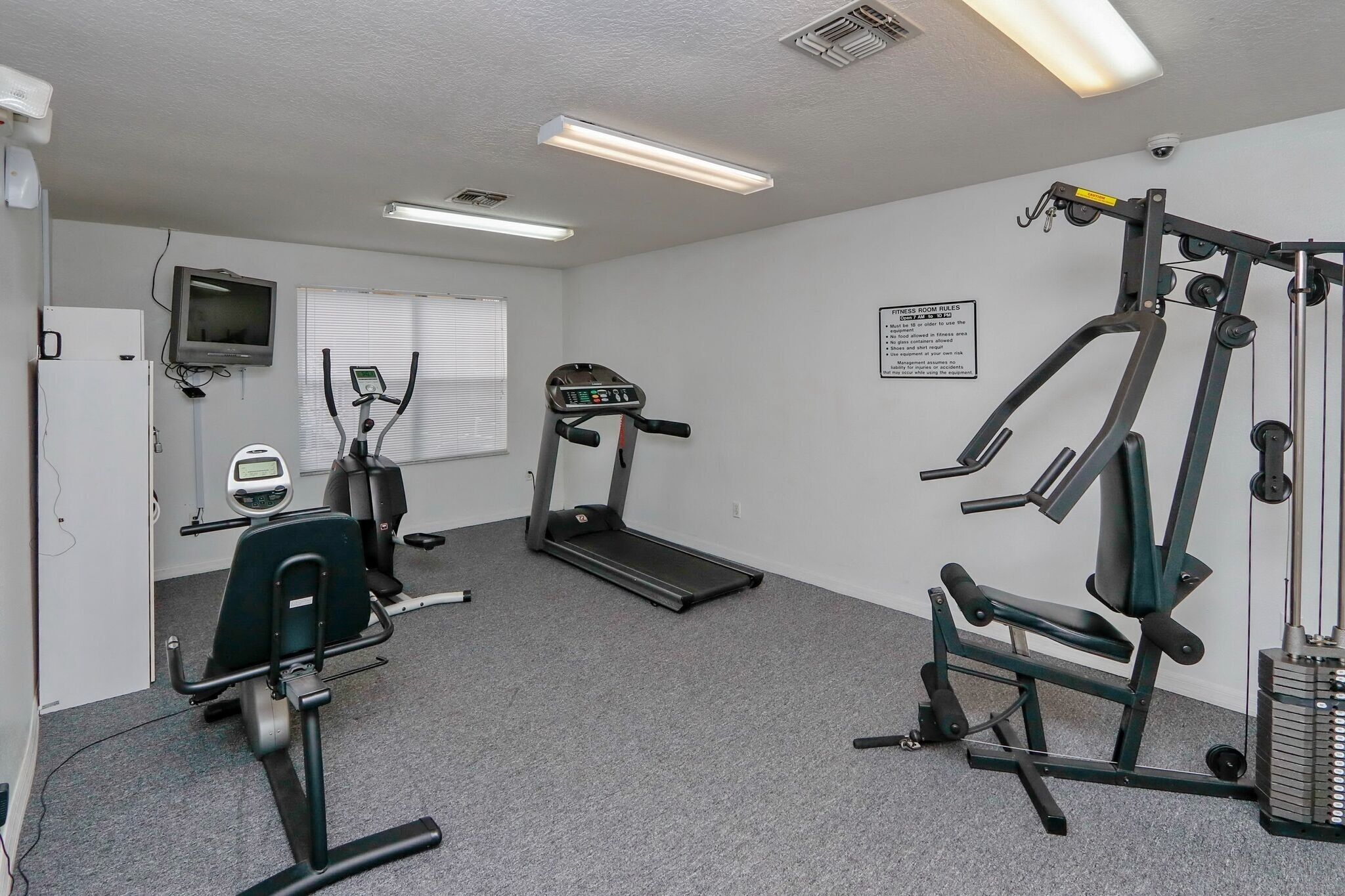 Une salle de sport équipée de tapis de course, d’appareils de musculation et d’un téléviseur fixé au mur.