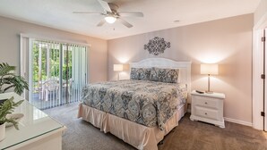 Quarto com uma cama grande, um ventilador de teto, uma mesa de cabeceira com abajur e vista para o exterior por uma porta deslizante.