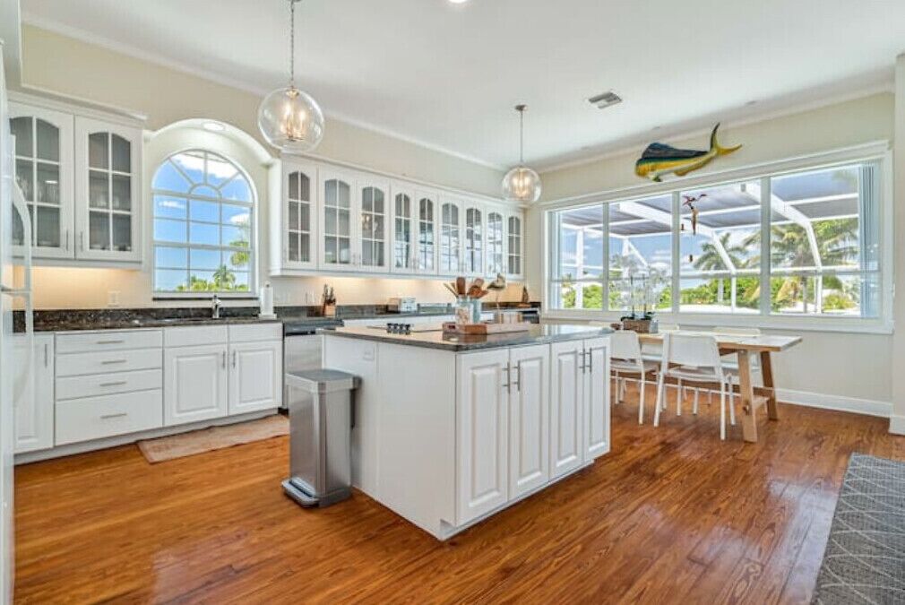 A spacious kitchen with white cabinetry, a central island, and large windows offering views of the outdoors.