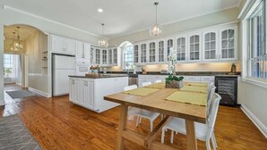 Une cuisine spacieuse avec des meubles blancs, une table Ă manger en bois et des luminaires suspendus.