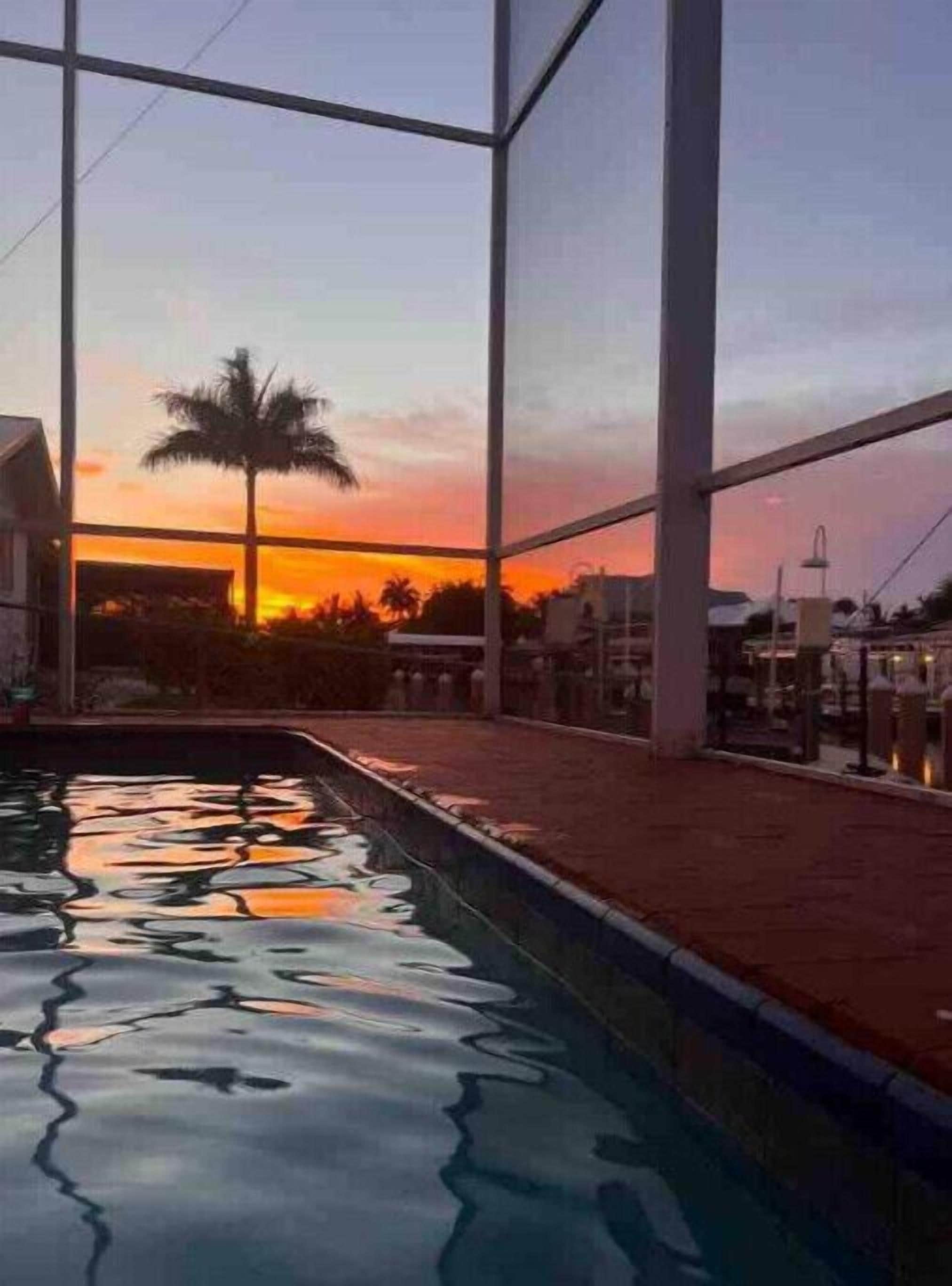 Ein Schwimmbad mit Blick auf einen Sonnenuntergang durch große Fenster.
