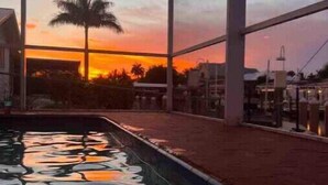 Une piscine avec vue sur le coucher de soleil, grĂące Ă de grandes fenĂȘtres.