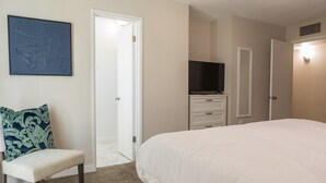 Een slaapkamer met een groot bed, een stoel, een televisie en een deur naar een andere kamer.