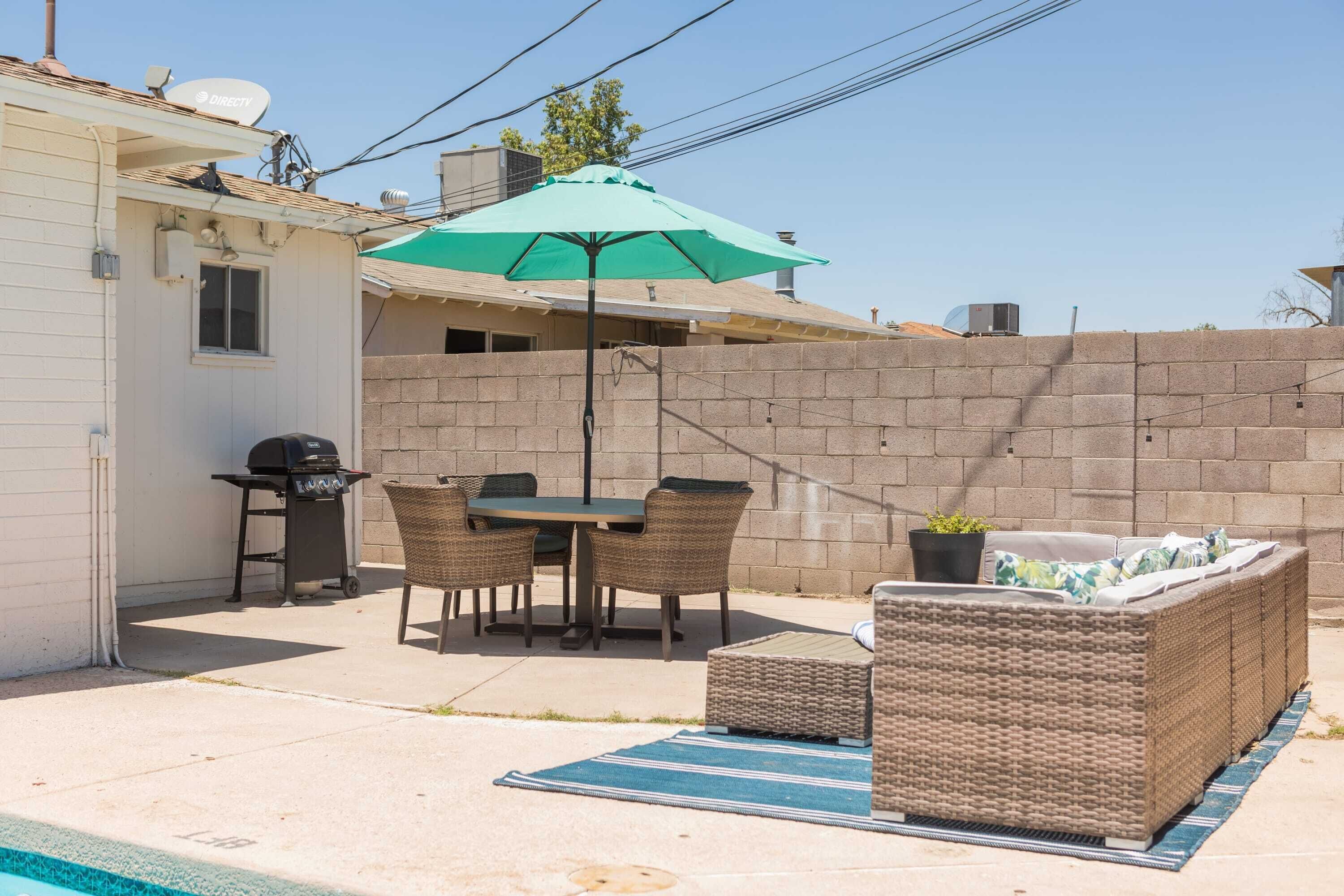 Un patio trasero con área de terraza, una parrilla y mobiliario exterior.