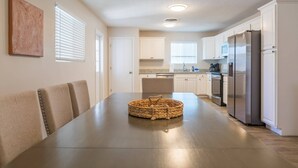 Een moderne keuken met witte kasten, roestvrijstalen apparatuur en een eethoek met een donkere tafel en stoelen.