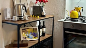 A kitchen with a gas stove, a coffee maker, a framed picture, a vase with red flowers, and wine bottles on a shelf. - Welcome "Casa San Gimi" your perfect base for exploring the wonders of Tuscany!  (San Gimignano)