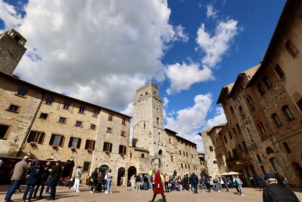 A historic square with a prominent tower, stone buildings, and a crowd of people.