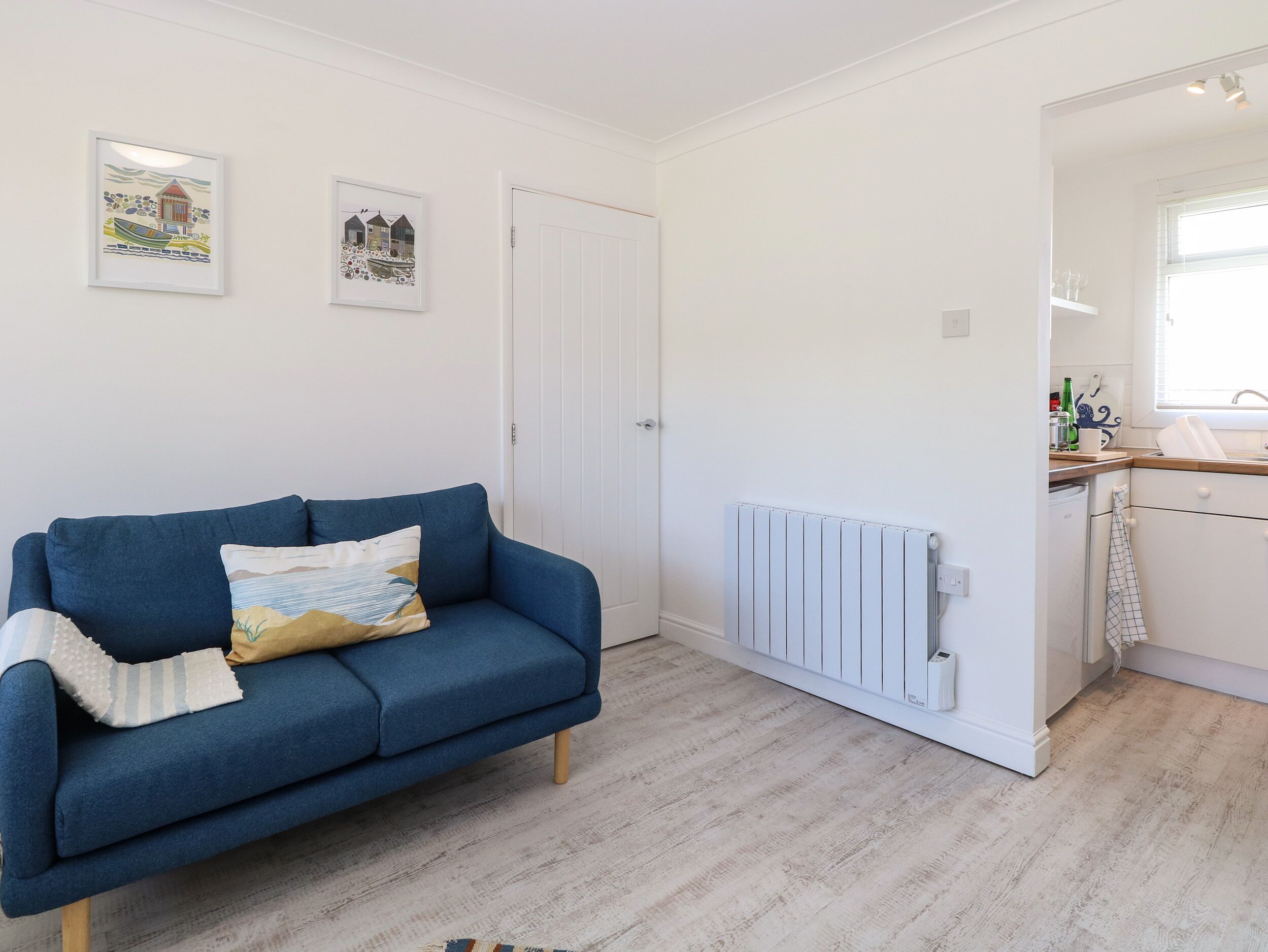 A room with a blue sofa, a white radiator, and a kitchen area with a window.
