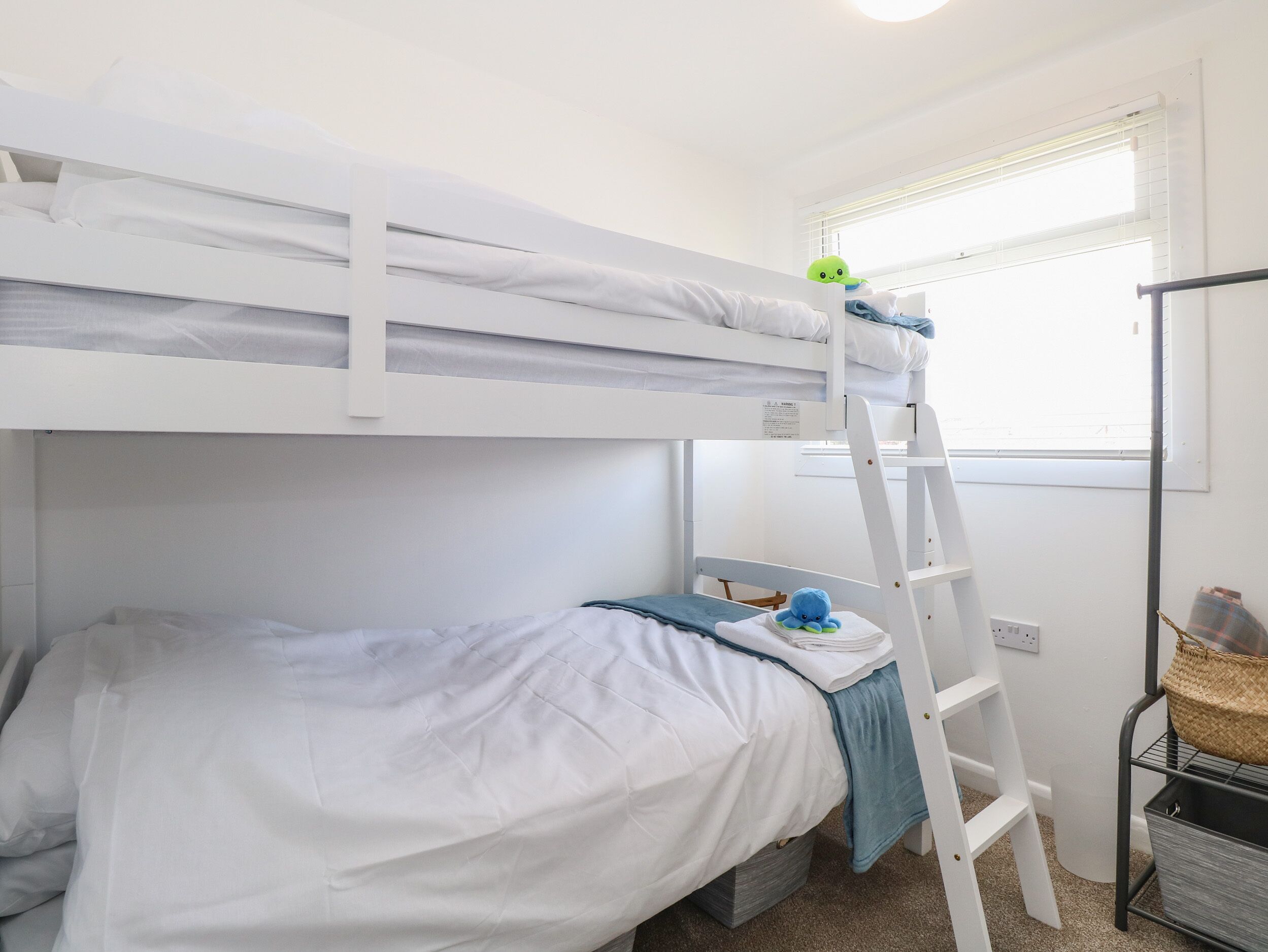 Een slaapkamer met stapelbed, een ladder, een raam en een klein plankje met een mandje.