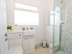 A modern bathroom with a white sink, mirror, and toilet. There is a glass shower enclosure and a small trash bin. - Dolly's Lookout (Lowestoft)