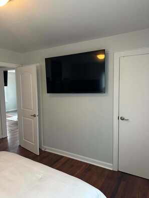 Un dormitorio con cama, televisor montado en la pared y una puerta.