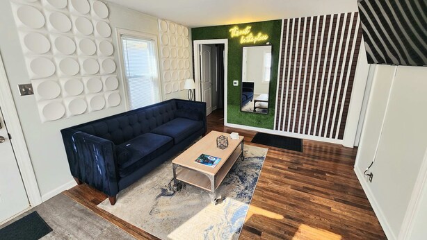 Uma sala de estar moderna com um sofá azul escuro, uma mesa de centro de madeira e um tapete estampado.