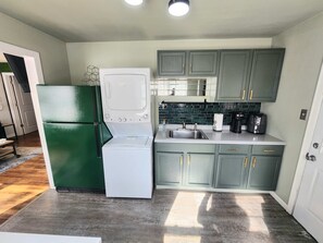 A compact kitchen with a refrigerator, washer, microwave, sink, and coffee maker.