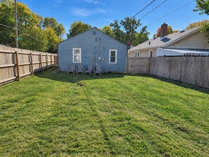 A residential backyard with a blue house, a wooden fence, and a grassy lawn.