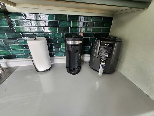 A kitchen with a green tiled backsplash, a paper towel dispenser, a coffee maker, and a water dispenser.