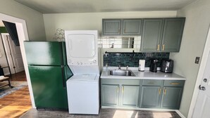 Cozinha compacta com geladeira, máquina de lavar, micro-ondas, pia e cafeteira.