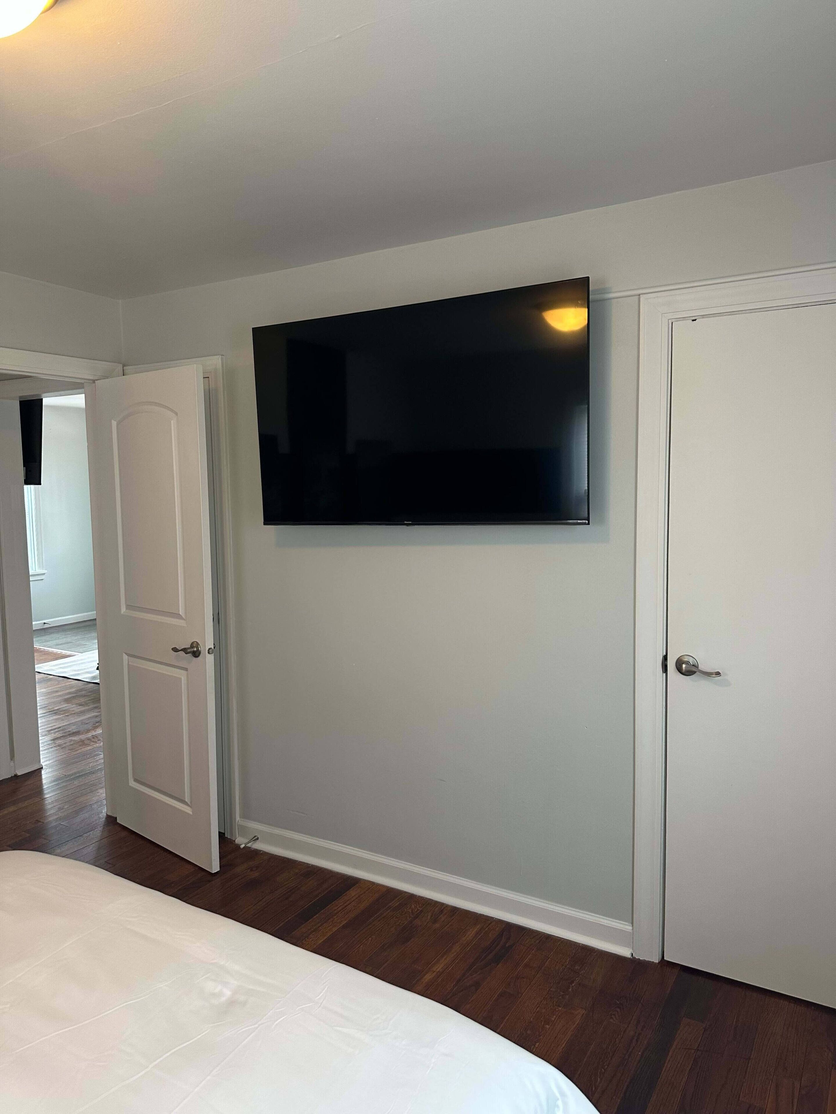 A bedroom with a bed, a TV mounted on the wall, and a door.