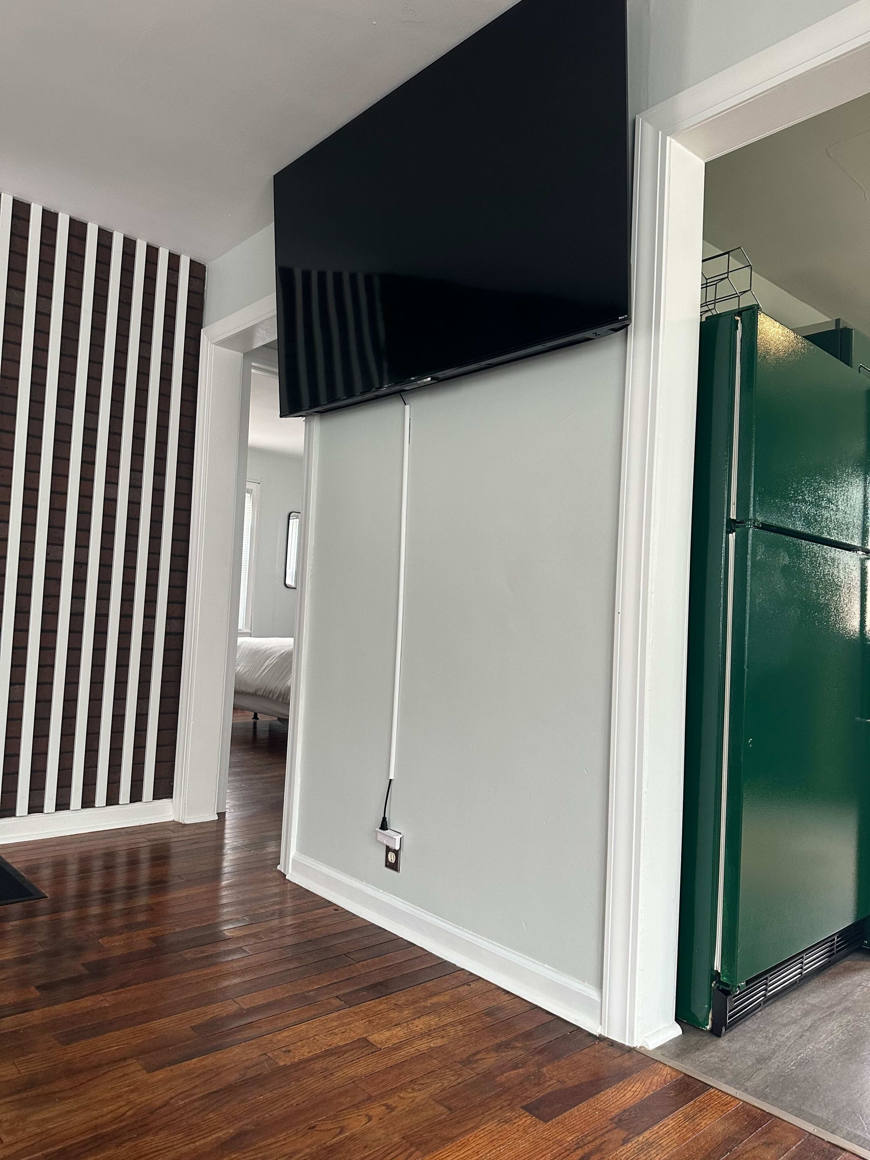 A hallway with a wooden floor, a black TV mounted on a white wall, and a green refrigerator.