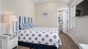 A bedroom with a bed, nightstand, lamp, ceiling fan, and a door leading to a bathroom. - The Lighthouse -Steps to Beach!  Luxury Amenities! (Corolla)